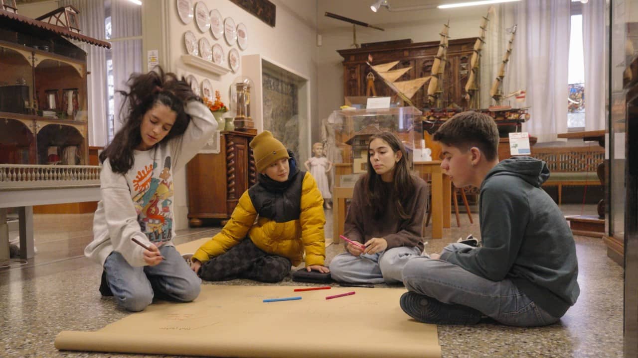 vier Schülerinnen und Schüler sitzen im Museum auf dem Boden