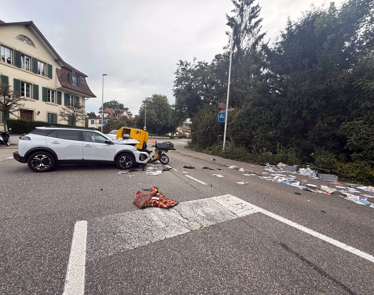 Weisses Fahrzeug auf Strasse mit Postkleinmotorfahrrad kollidiert. Post auf der Strasse verteilt.