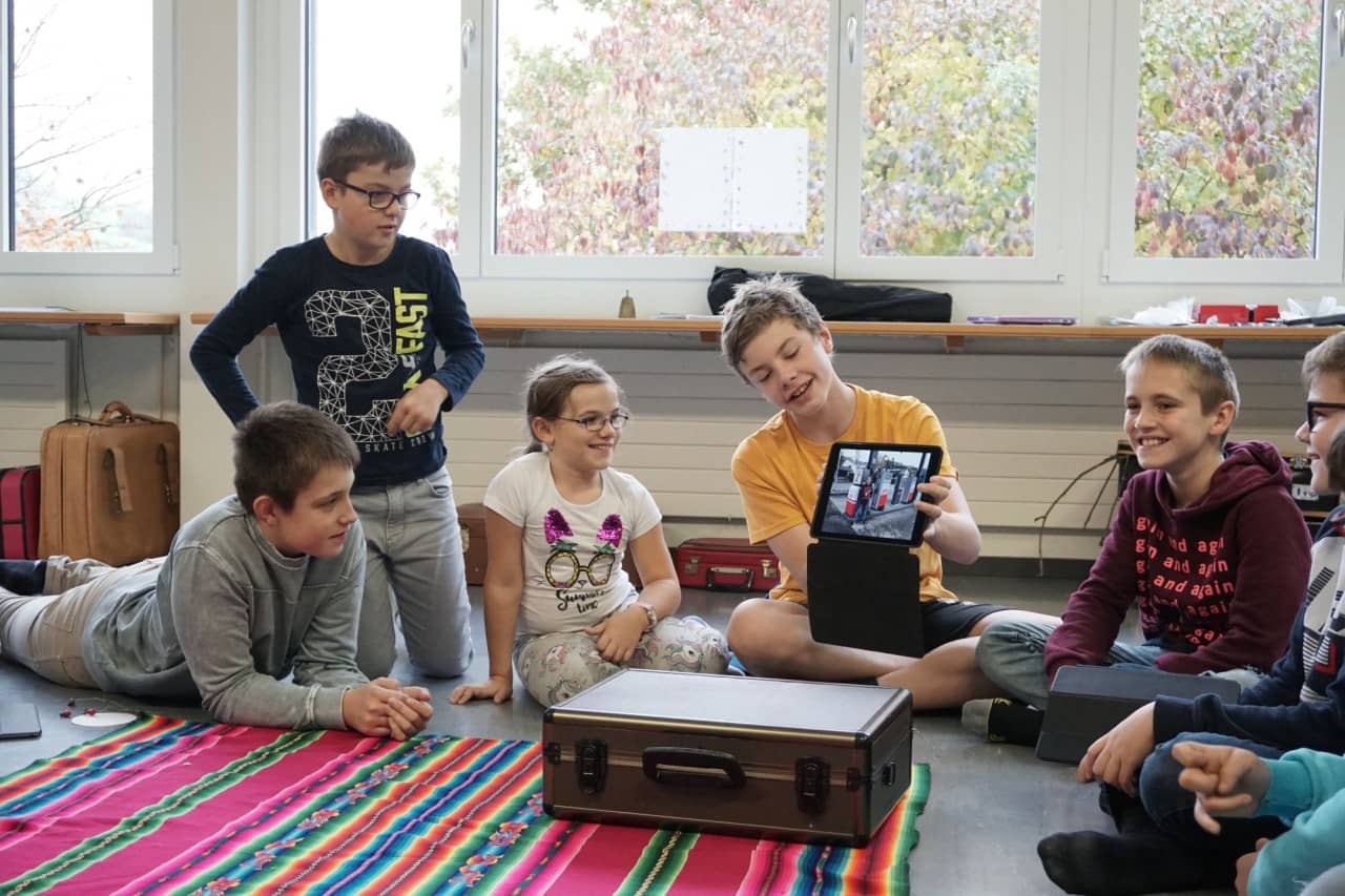 Schülerinnen und Schüler sitzen versammelt um ein Tablet