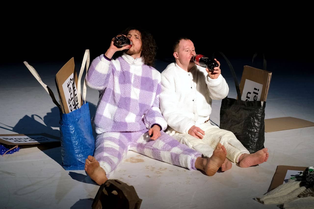 Zwei Personen sitzen am Boden und trinken aus einer Flasche. 