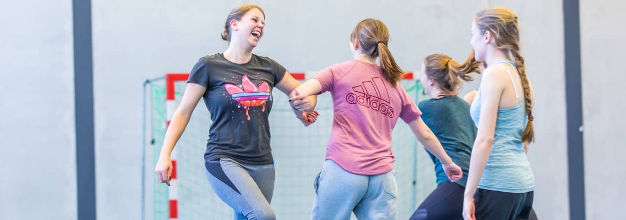 Mehrere junge Frauen üben Sport in der Turnhalle aus.