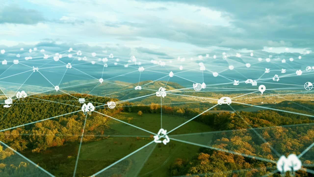 Blick auf eine hügelige, bewaldete Landschaft über der Punkte mit Symbolen wie z.B. Bäumen, Elektroautos, Globus, etc. liegen. Die Icons sind mittels feiner Linien miteinander verbunden.